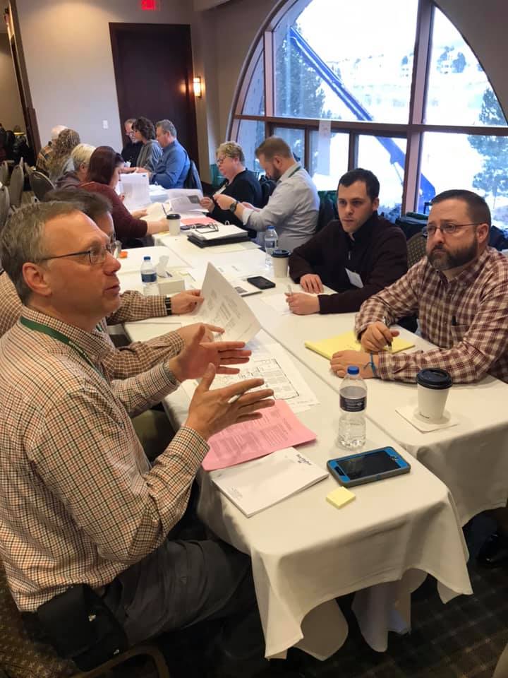 Two groups of people sitting at tables looking through papers and talking to each other.